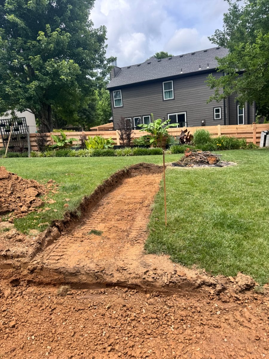 Utility trench cut across a green lawn in red dirt